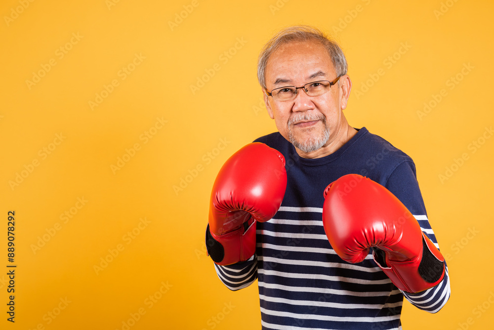 Portrait Asian old man wearing glasses wear two red boxing gloves studio shot isolated yellow background, smiling happy elderly man gray haired healthy fighter lifestyle concept Portrait Asian old man wearing glasses wear two red boxing gloves studio shot isolated yellow background, smiling happy elderly man gray haired healthy fighter lifestyle concept