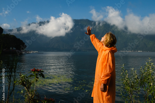 Solo Traveler in Orange Raincoat Admiring Serene Mountain Lake View in Nature.