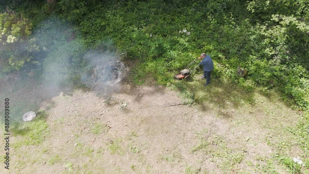 Aerial view of a man clearing overgrown garden with a fire burning nearby Aerial view of a man clearing overgrown garden with a fire burning nearby