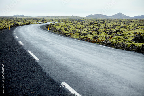A curving asphalt road surrounded by a rugged lava rock landscape under a cloudy sky. Iceland