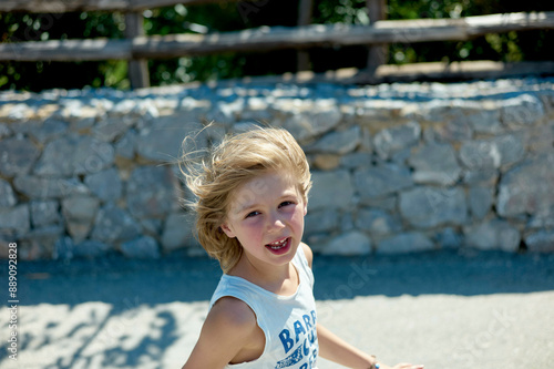 Smiling young child with blond hair running outdoors on a sunny day.