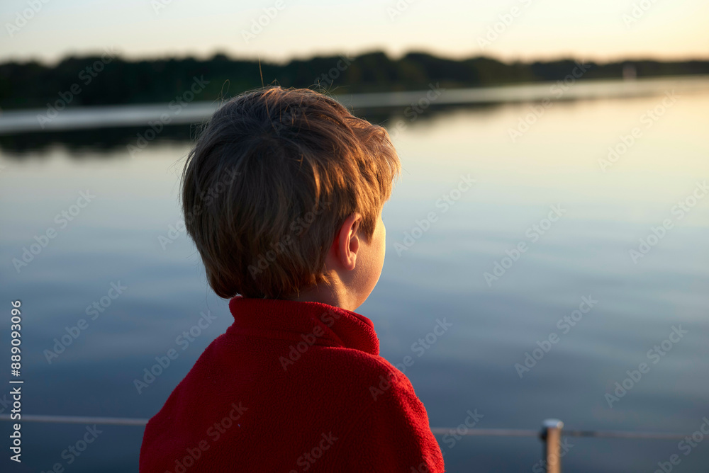 Child in red sweater enjoying a serene lakeside view at sunset. Child in red sweater enjoying a serene lakeside view at sunset.