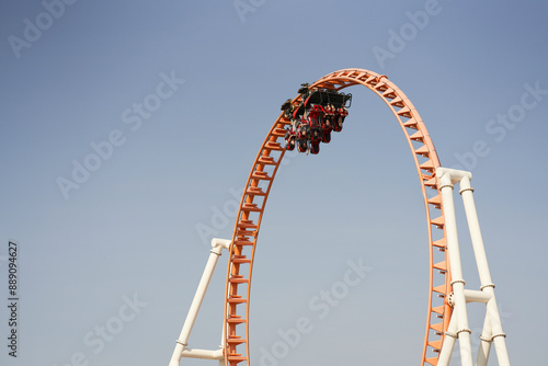Roller coaster at the peak of a loop against a clear blue sky.