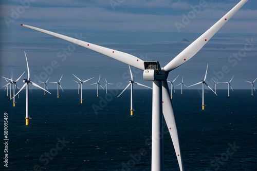Offshore wind turbines stand tall over a calm blue sea under a clear sky.