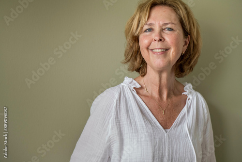 A smiling middle-aged woman in a white blouse looking away from the camera with a soft beige background.