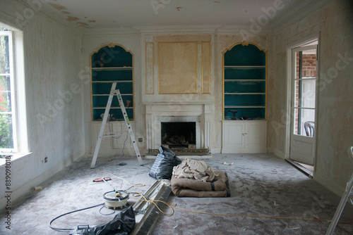 An interior view of a room undergoing renovation with tools and a ladder present, exposed wall sockets, and a fireplace.