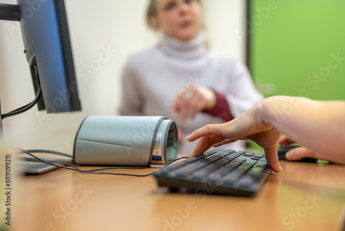 A person's hand is typing on a keyboard with a view of a blurred colleague in the background. photo