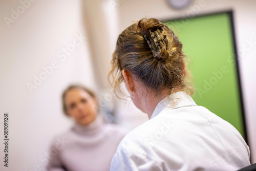 A woman with her hair up in a clip is seen from behind, in focus, with another woman out of focus in the background. photo