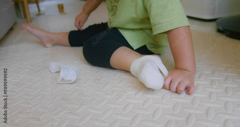 A close-up of little child trying to Put on Socks While Sitting on floor in a Cozy living room at Home A close-up of little child trying to Put on Socks While Sitting on floor in a Cozy living room at Home
