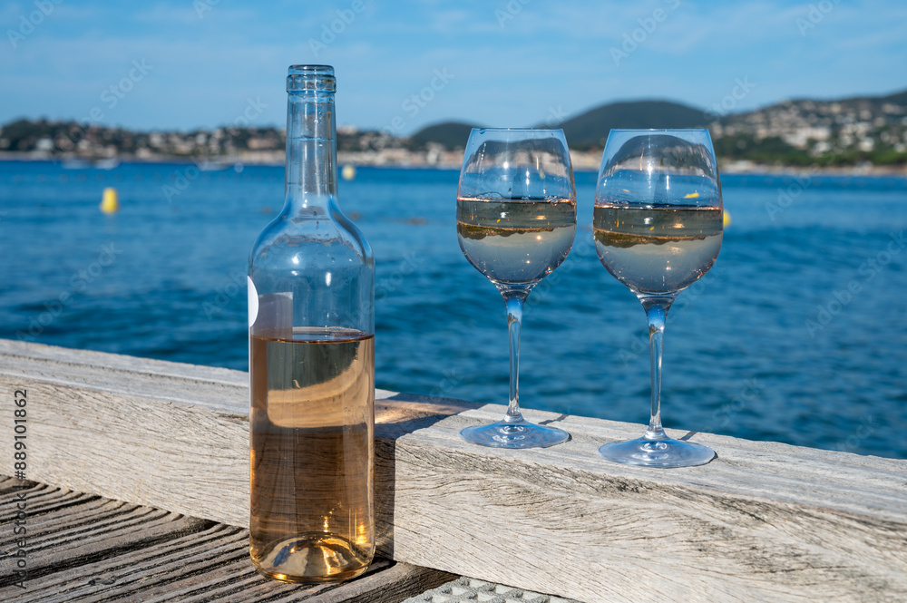 Tasting of cold rose wine from Provence outdoor on wooden yacht pier with view on blue water and white sandy beach Plage de Pampelonne near Saint-Tropez, summer vacation in France Tasting of cold rose wine from Provence outdoor on wooden yacht pier with view on blue water and white sandy beach Plage de Pampelonne near Saint-Tropez, summer vacation in France
