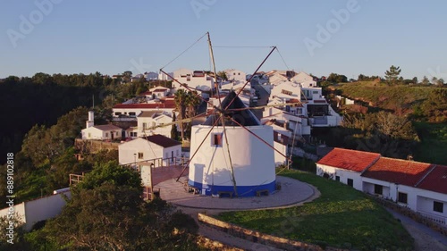 Aerial view of charming traditional village with windmill, red roofs, and greenery, Odeceixe, Portugal.