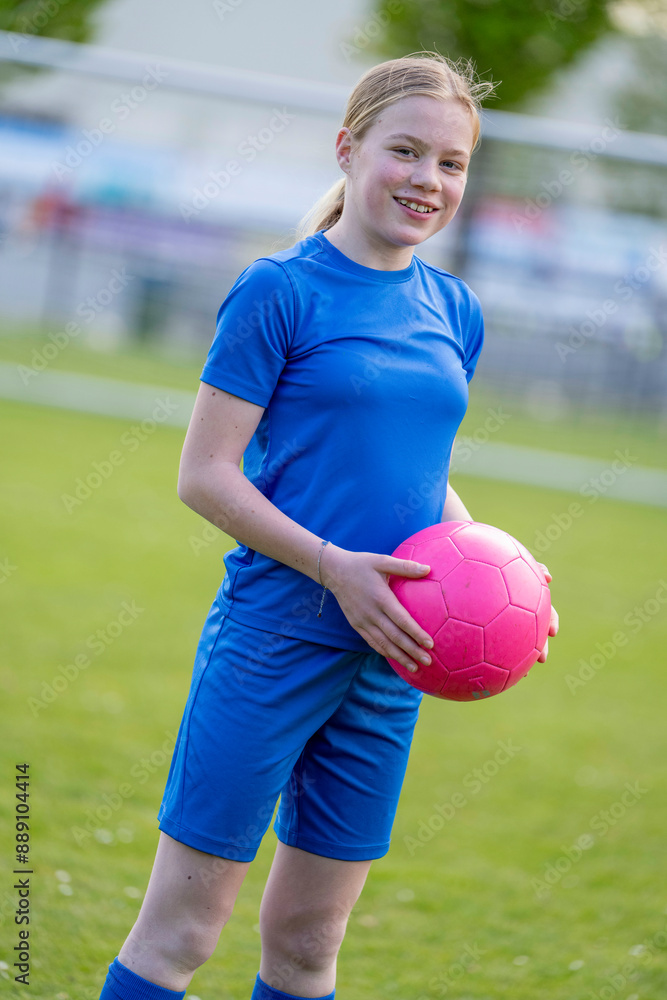 Smiling teenage girl in blue sportswear holding a pink soccer ball in a grassy field. Smiling teenage girl in blue sportswear holding a pink soccer ball in a grassy field.