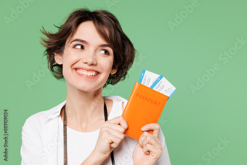 Traveler smiling woman wear casual clothes hold passport ticket look aside on area isolated on plain green background. Tourist travel abroad in free spare time rest getaway. Air flight trip concept. #889109034