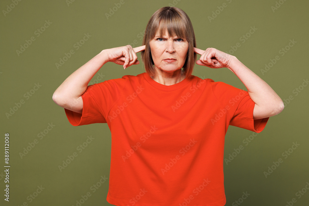 Elderly sad blonde woman 50s year old wear orange t-shirt casual clothes cover ears with hands fingers do not want to listen scream isolated on plain pastel green background studio. Lifestyle concept Elderly sad blonde woman 50s year old wear orange t-shirt casual clothes cover ears with hands fingers do not want to listen scream isolated on plain pastel green background studio. Lifestyle concept