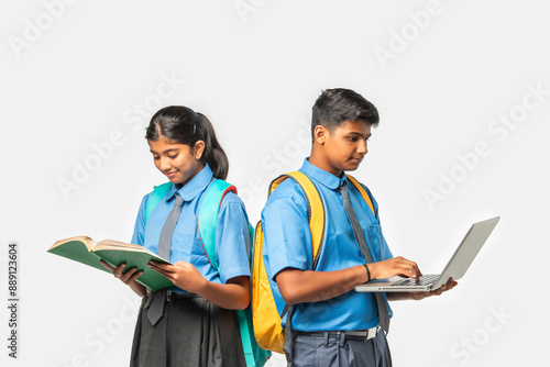 Asian Indian schoolboy and schoolgirl in uniforms, presenting blank space with books and backpacks