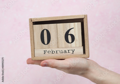 Wallpaper Mural Woman's hand holds wooden block calendar with the date February 06 on pink concrete background Torontodigital.ca