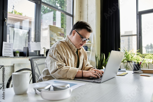 A young man with Down syndrome works on a laptop at a desk. photo