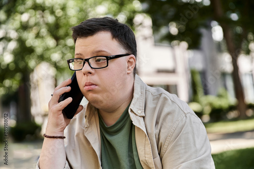 A man with Down syndrome sits outdoors and talks on a phone.