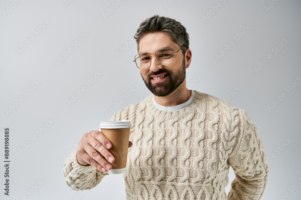 Bearded man in white sweater holds a steaming coffee cup in a cozy studio setting on a grey background. Bearded man in white sweater holds a steaming coffee cup in a cozy studio setting on a grey background.