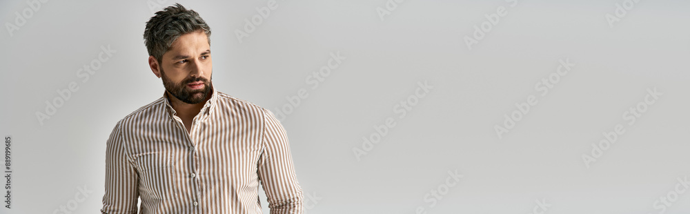 Obraz premium A stylish man with an alluring beard poses confidently in elegant attire against a sleek white backdrop.