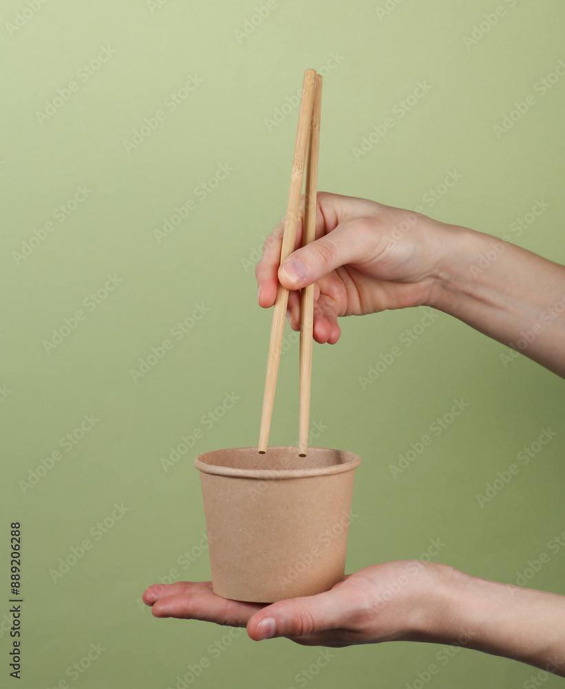 Hands holding a package of takeaway food with Chinese chopsticks on a green background Hands holding a package of takeaway food with Chinese chopsticks on a green background