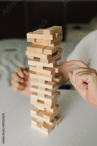 A father and son play a block tower game together indoors. The game is taking place on a white table, and the background is out of focus. Father's day