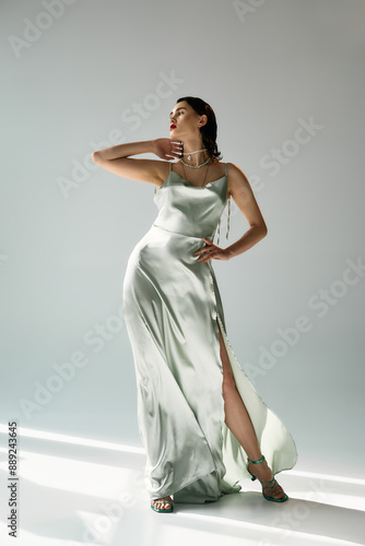 Slika na platnu A young, beautiful woman with red lips posing in a white dress and gloves in a studio on a grey background