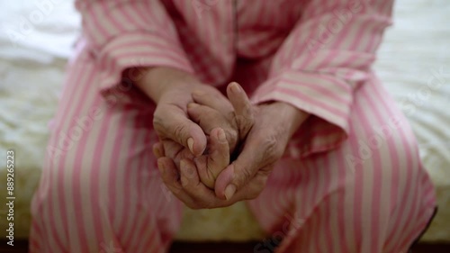 Close-up of the hands of an old woman dressed in pajamas and sitting on her bed. Concept of loneliness in retirement 4K