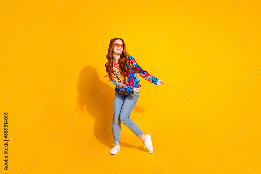 Full size photo of nice girl dressed print shirt jeans dancing in sunglass look at sale empty space isolated on yellow color background Full size photo of nice girl dressed print shirt jeans dancing in sunglass look at sale empty space isolated on yellow color background