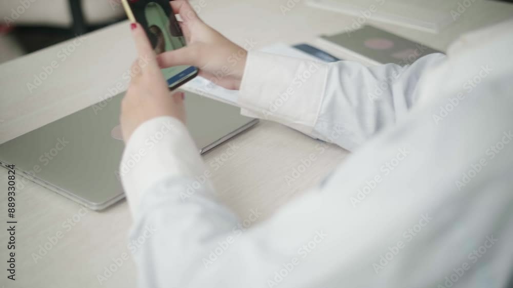 A scene from a video showing an Asian woman arriving at the office and using her phone to record her attendance. She appears focused as she interacts with the phone screen. A scene from a video showing an Asian woman arriving at the office and using her phone to record her attendance. She appears focused as she interacts with the phone screen.