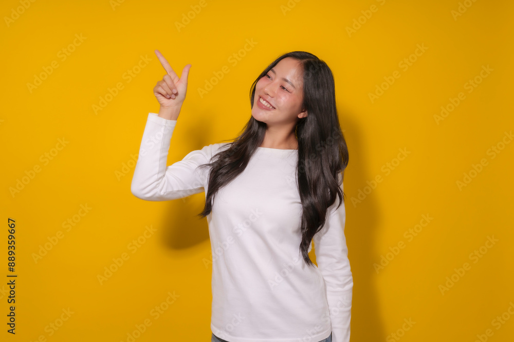 Young asian woman smiling and pointing in a studio with a yellow background, perfect for ads or marketing. Her inviting gesture suggests she's presenting a product or service Young asian woman smiling and pointing in a studio with a yellow background, perfect for ads or marketing. Her inviting gesture suggests she's presenting a product or service