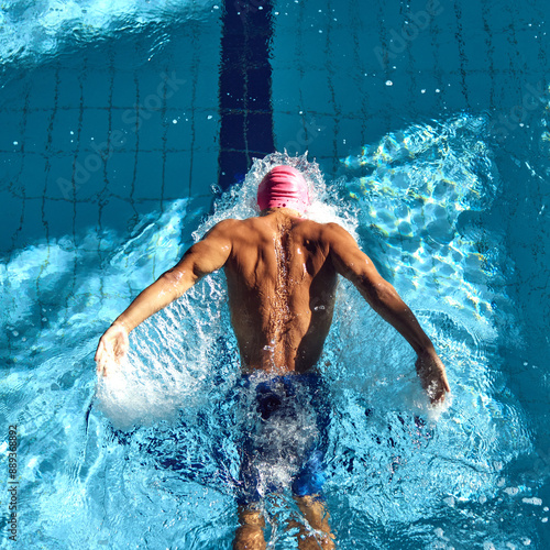 Konstfotografi Overhead view swimmer in pink cap performs powerful butterfly stroke, his back muscles rippling with each stroke in clear blue pool
