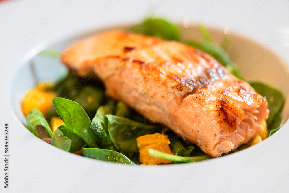 Seared salmon fillet on a bed of spinach and orange cubes in a deep white plate Seared salmon fillet on a bed of spinach and orange cubes in a deep white plate