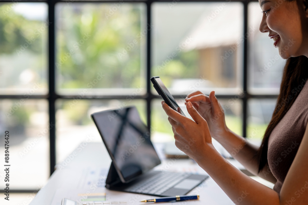 A woman is sitting at a desk with a laptop and a cell phone A woman is sitting at a desk with a laptop and a cell phone