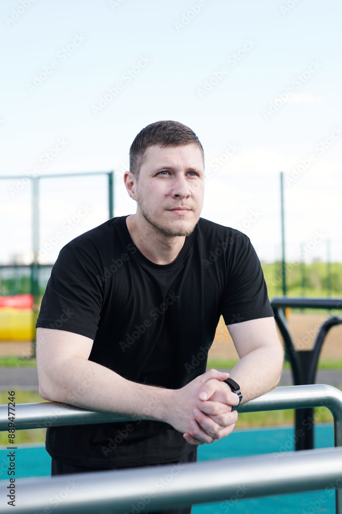 A male athlete is training on the sports ground outside. Caucasian male rests between approaches to workout outdoors in summer park A male athlete is training on the sports ground outside. Caucasian male rests between approaches to workout outdoors in summer park