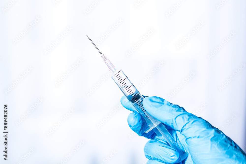 Human hand wearing medical gloves holds a syringe needle,Doctor hands with syringe on light background Human hand wearing medical gloves holds a syringe needle,Doctor hands with syringe on light background
