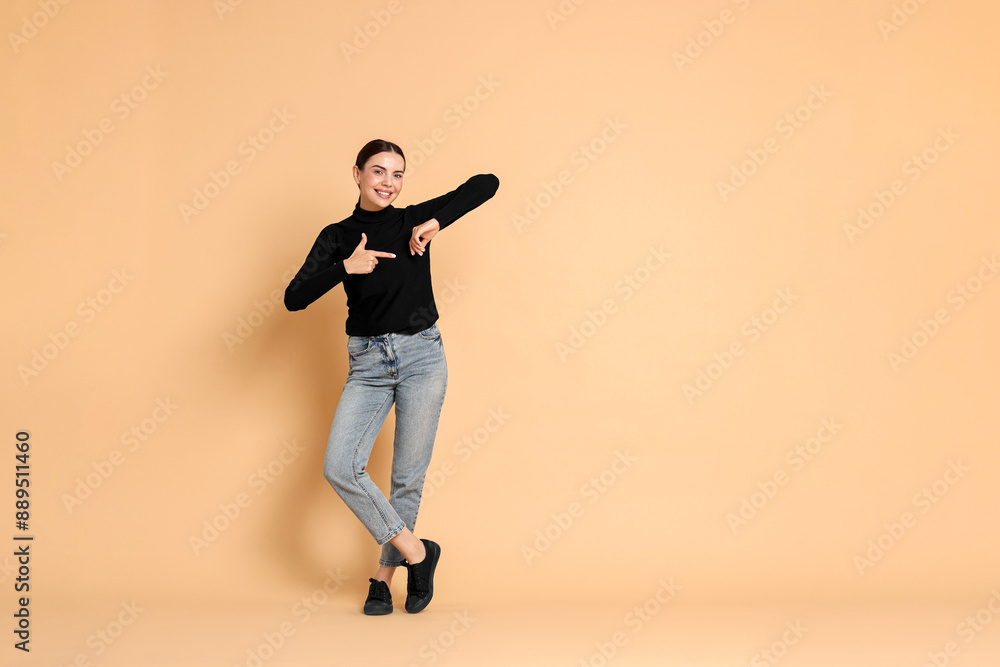 Smiling woman pointing at something on beige background. Space for text Smiling woman pointing at something on beige background. Space for text