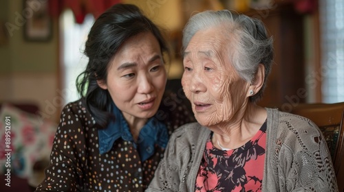 Asian caregiver gently assisting an elderly woman with arm exercises in a cozy home setting, focusing on elderly care and physical therapy © Pravinrus