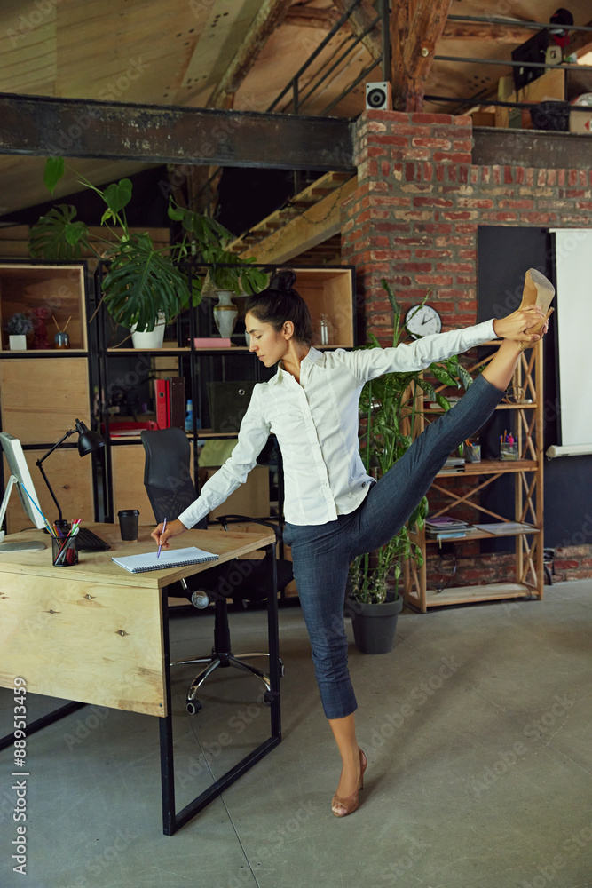 Promoting healthy and active lifestyle in modern office setting. Woman standing at her desk and doing stretching activity. Concept of office life, balance between work and sport, business Promoting healthy and active lifestyle in modern office setting. Woman standing at her desk and doing stretching activity. Concept of office life, balance between work and sport, business