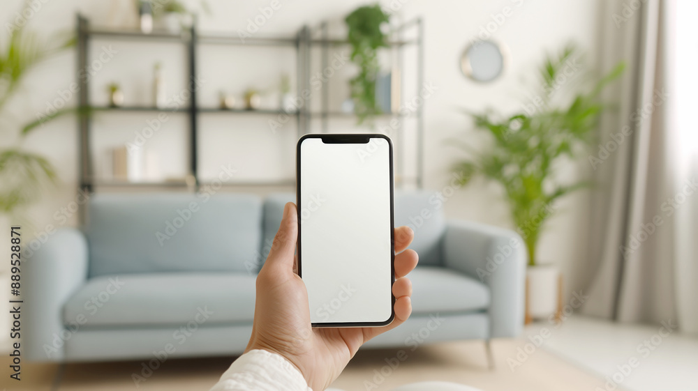 A person holding a mobile phone with a mockup screen, in a cozy living room with modern furniture and plants. A person holding a mobile phone with a mockup screen, in a cozy living room with modern furniture and plants.