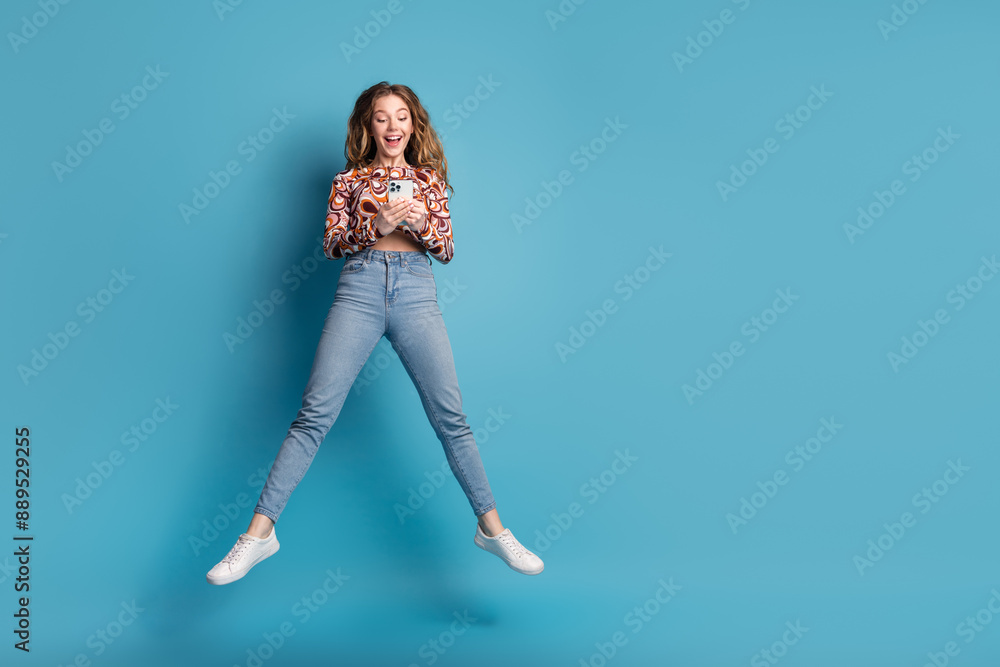 Full length portrait of nice young girl jump smart phone wear top isolated on blue color background Full length portrait of nice young girl jump smart phone wear top isolated on blue color background