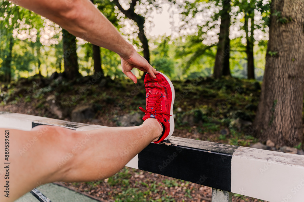 Fototapeta premium Close-up of a runner in red sneakers stretching his legs before training