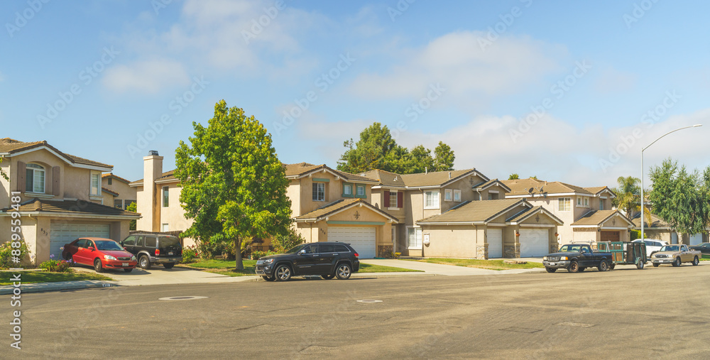 Obraz premium Beautiful houses with nicely landscaped front the yard, and cars parked on a sidewalk.