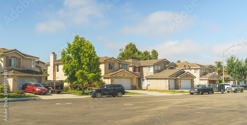 Beautiful houses with nicely landscaped front the yard, and cars parked on a sidewalk.