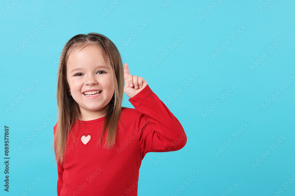 Portrait of happy little girl pointing at something on light blue background, space for text Portrait of happy little girl pointing at something on light blue background, space for text