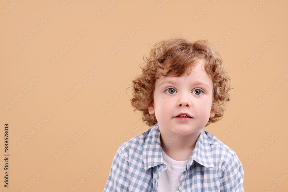 Portrait of cute little boy on beige background, space for text