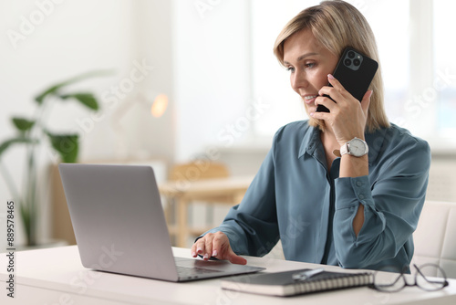 Happy woman using mobile phone at white table indoors