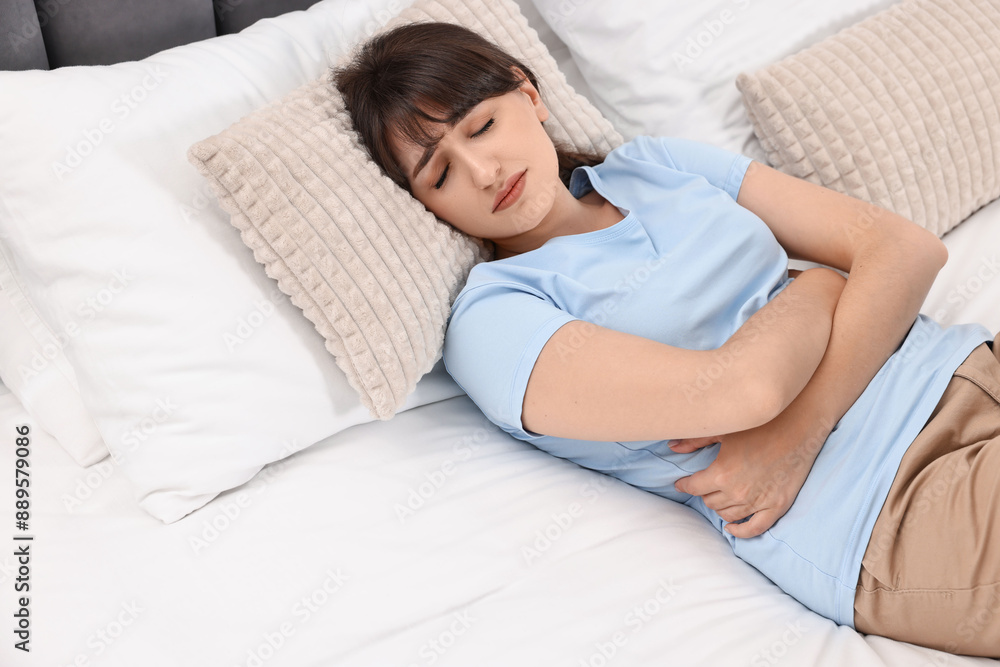 Upset woman suffering from abdominal pain on bed at home Upset woman suffering from abdominal pain on bed at home