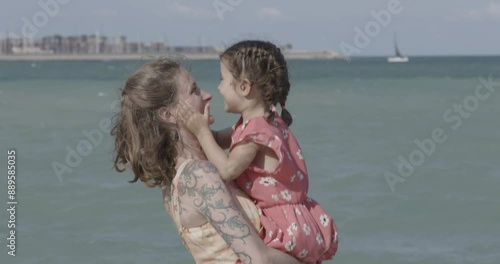 Smiling mother and daughter jumping and kissing each other by the sea