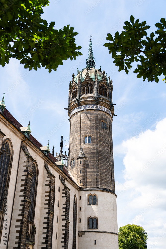 Nave of the Castle Church in Wittenberg with castle tower. Church hymn surrounds the tower. Portrait format photo of the castle tower framed by leaves.